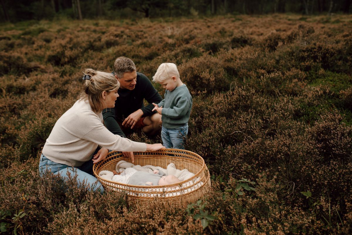 Drie mensen knielen in een grasveld en delen brood uit een rieten mand in een picknicktafereel.