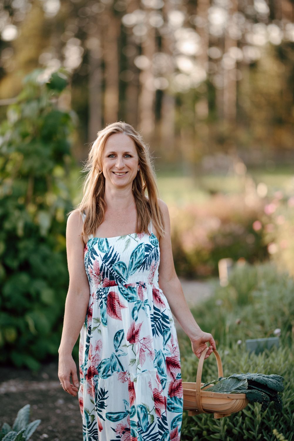Een vrouw in een gebloemde jurk houdt een mand vast in een tuin.