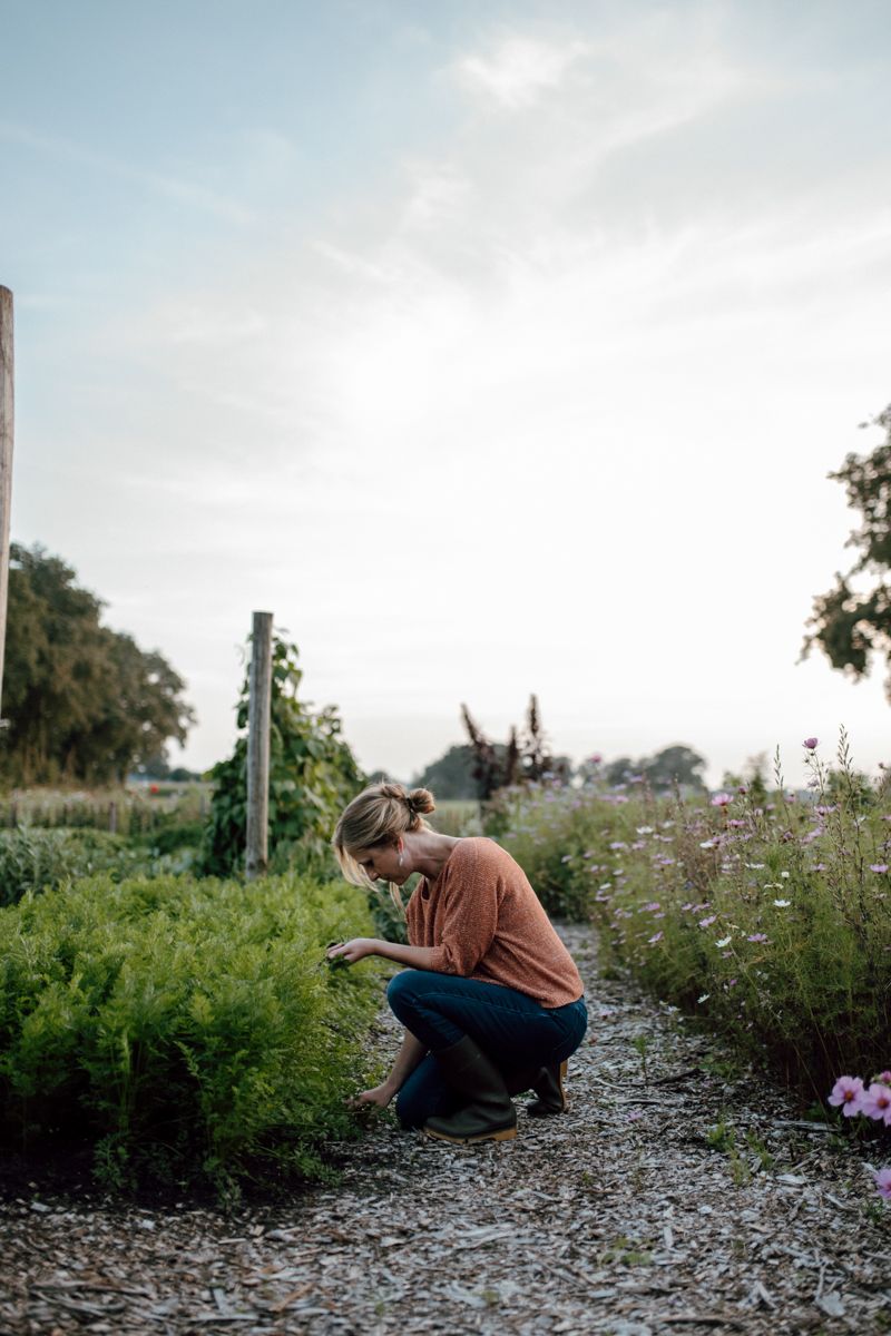 Een vrouw knielt in een tuin en kijkt naar planten.