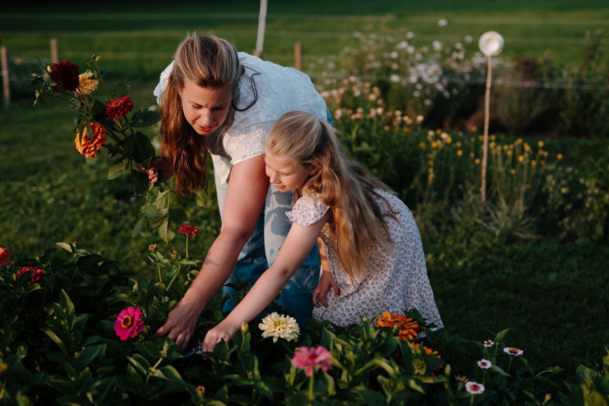 Een vrouw en een kind plukken samen kleurrijke bloemen in een zonnige tuin.
