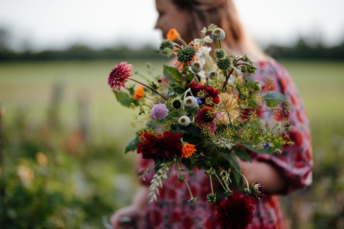 Een persoon in een jurk met een patroon houdt een levendig, gevarieerd boeket kleurrijke bloemen vast in een tuin.
