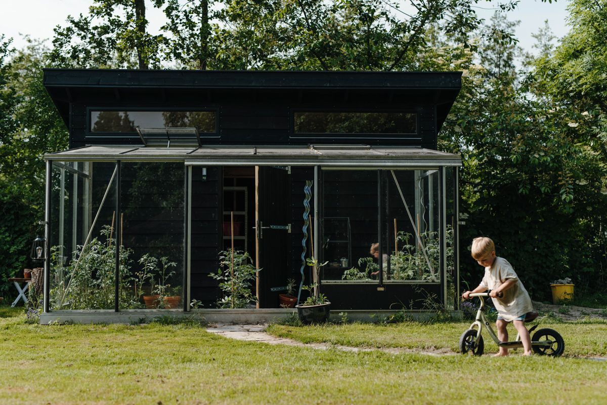 Jongetje op zijn loopfiets voor de kas tijdens een fotoshoot in de tuin