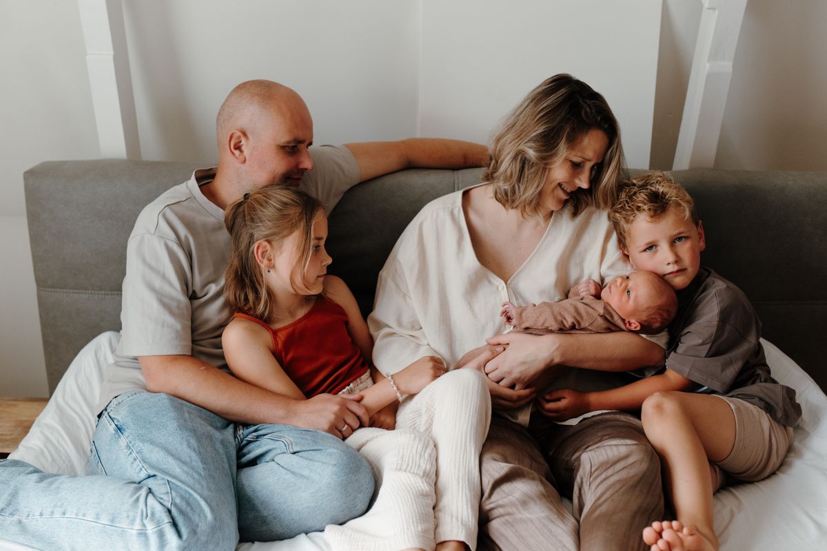 Een gezin, bestaande uit twee volwassenen en twee kinderen, zit gezellig samen op de bank in een knusse woonkamer.