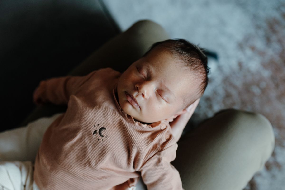 Een slapende baby in een roze outfit ligt op de schoot van een volwassene, met een zacht vervaagde achtergrond.