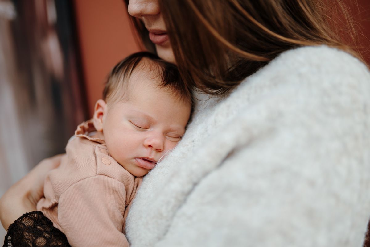 Een slapende baby, gewiegd in de armen van een vrouw, close-up met zachte, neutrale tinten.