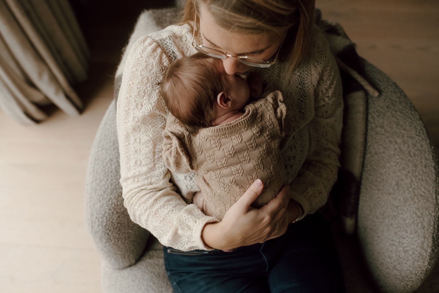 Een persoon, gekleed in een crèmekleurige trui met structuur, houdt een pasgeboren baby voorzichtig vast en kust hem op het voorhoofd.