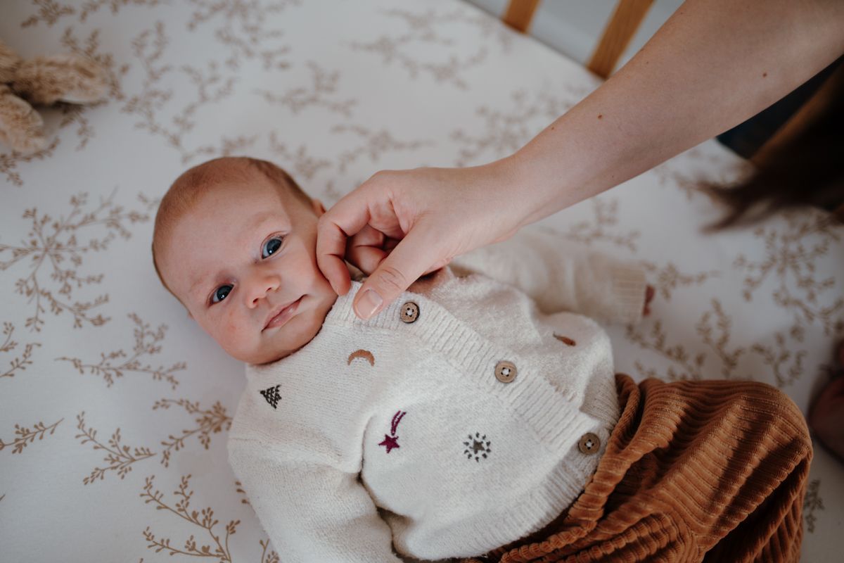 Een baby ligt op een dekentje met een patroon, terwijl een volwassen hand zachtjes over het wangetje streelt.