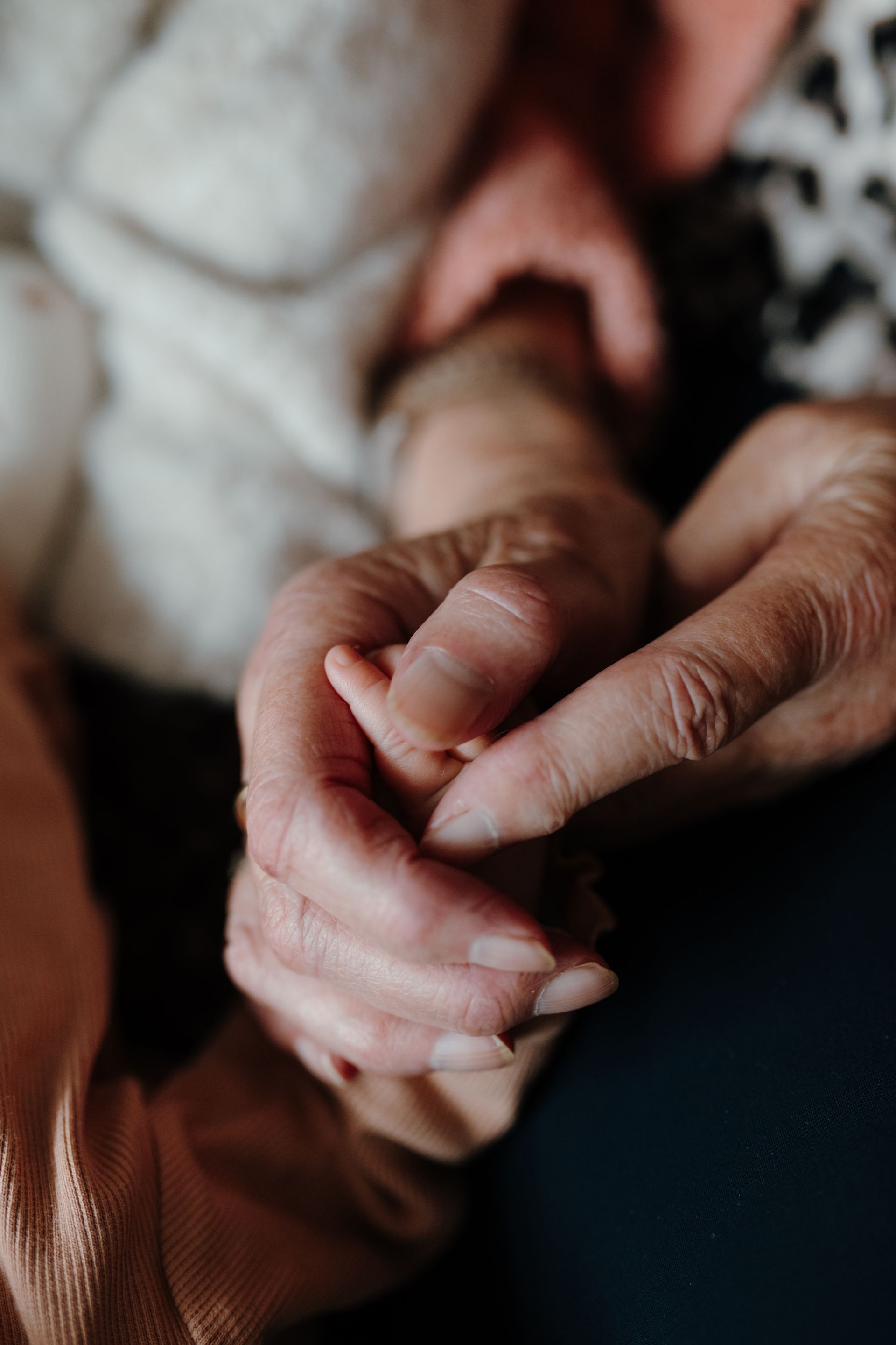 De hand van een oudere volwassene houdt voorzichtig het kleine handje van een baby vast.