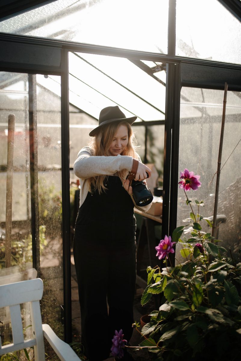 Een vrouw geeft bloemen water in een kas.