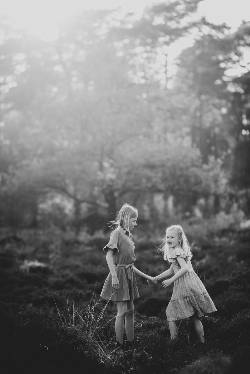 Twee kinderen lopen hand in hand door een veld met hoog gras tijdens zonsondergang.