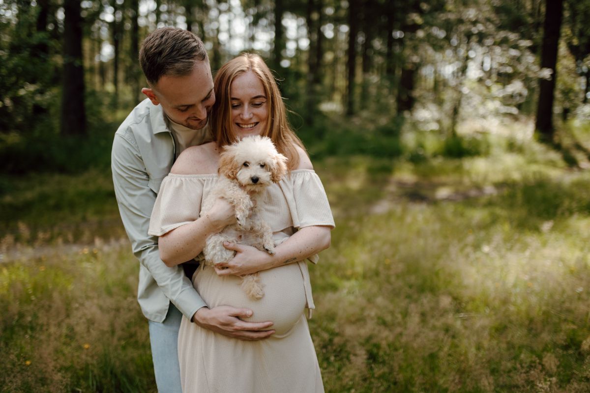 Een stel met een klein wit hondje in een zonnige open plek in het bos.
