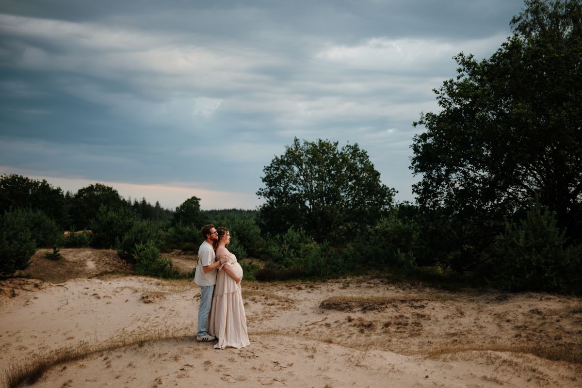 Aanstaande ouders omhelzen elkaar op een zandverstuiving bij Appelscha, natuurlijke zwangerschapsshoot