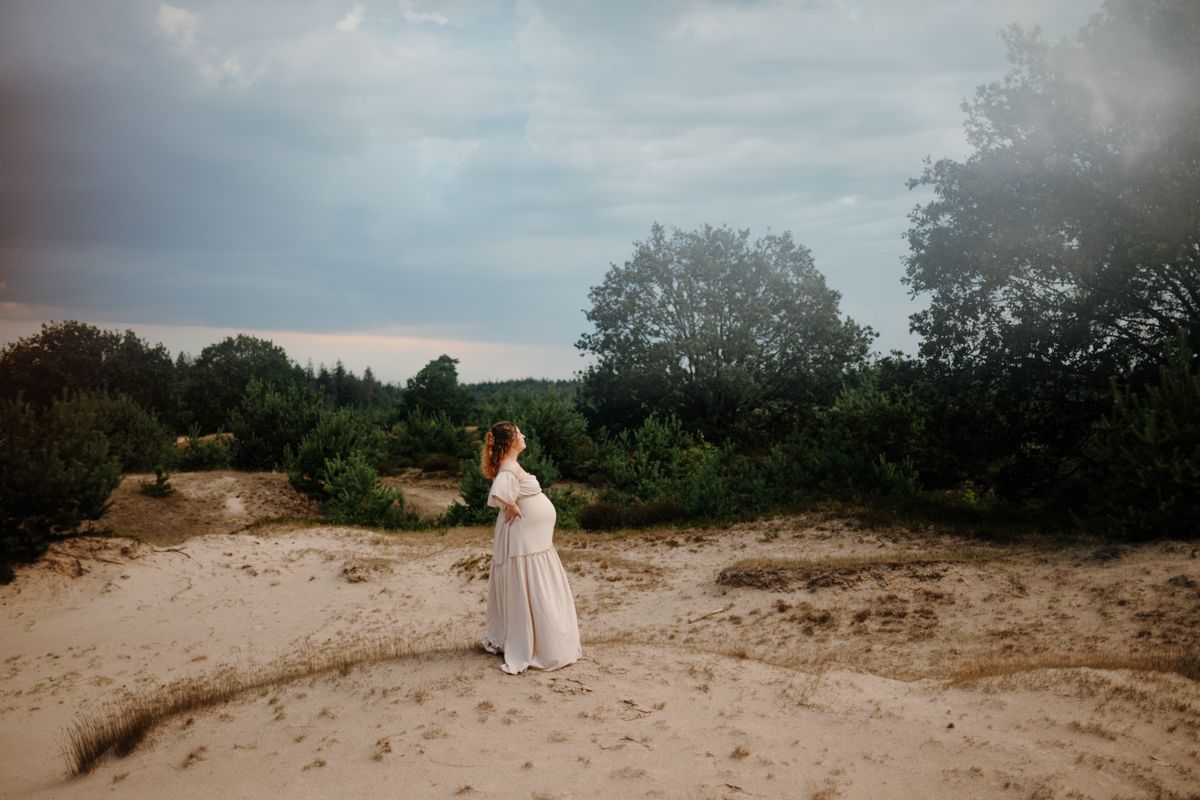 Zwangere vrouw in lange jurk op een zandduin in de natuur bij Appelscha, spontane zwangerschapsshoot