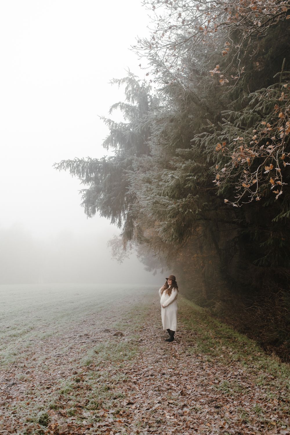 Zwangere vrouw staat onder de dennenbomen van de bossen van Beetsterzwaag, met mist op de achtergrond tijdens een fotoshoot