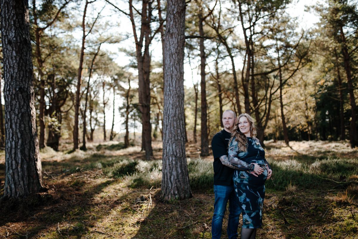 In een zonovergoten dennenbos staan ​​twee mensen achter elkaar, beiden met een glimlach.