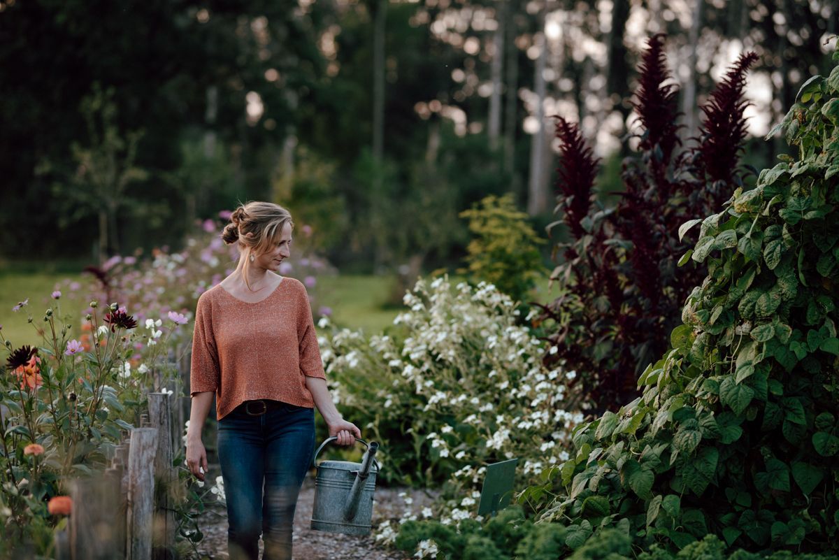 Een vrouw loopt door een tuin met een gieter in haar hand.