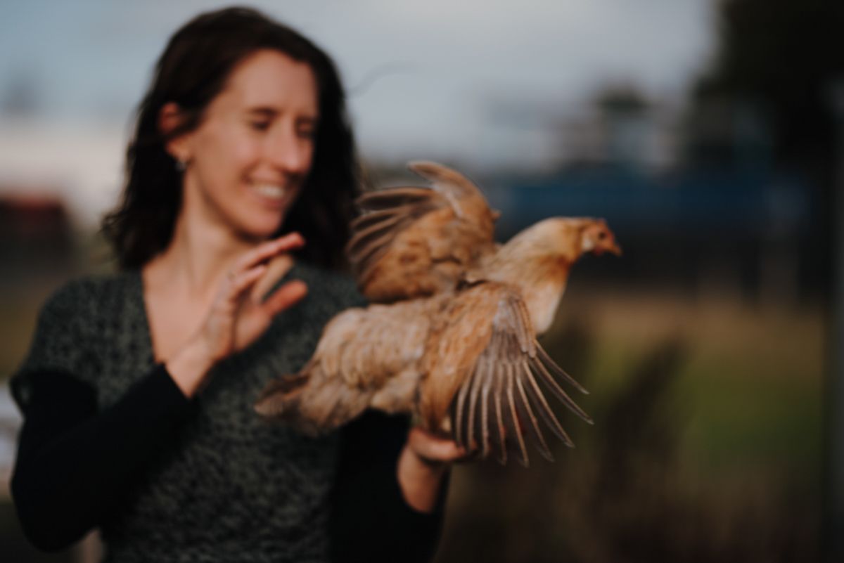 Een vrouw houdt een bruine kip in haar handen