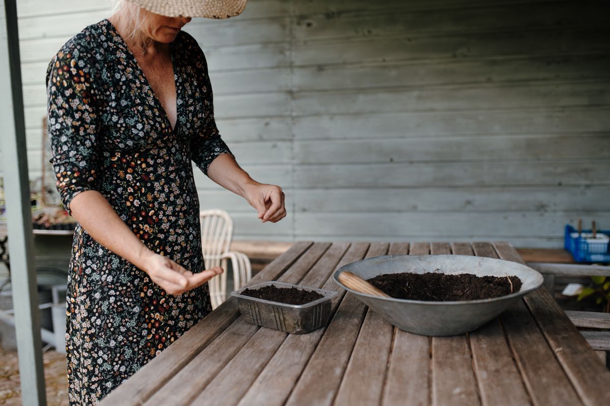 Een vrouw staat aan een tafel met een kom aarde erop