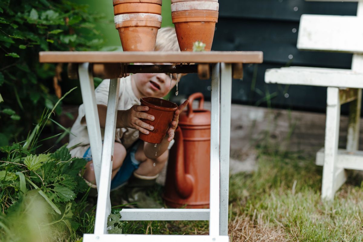 Een kleine jongen geeft potplanten water op een tafel