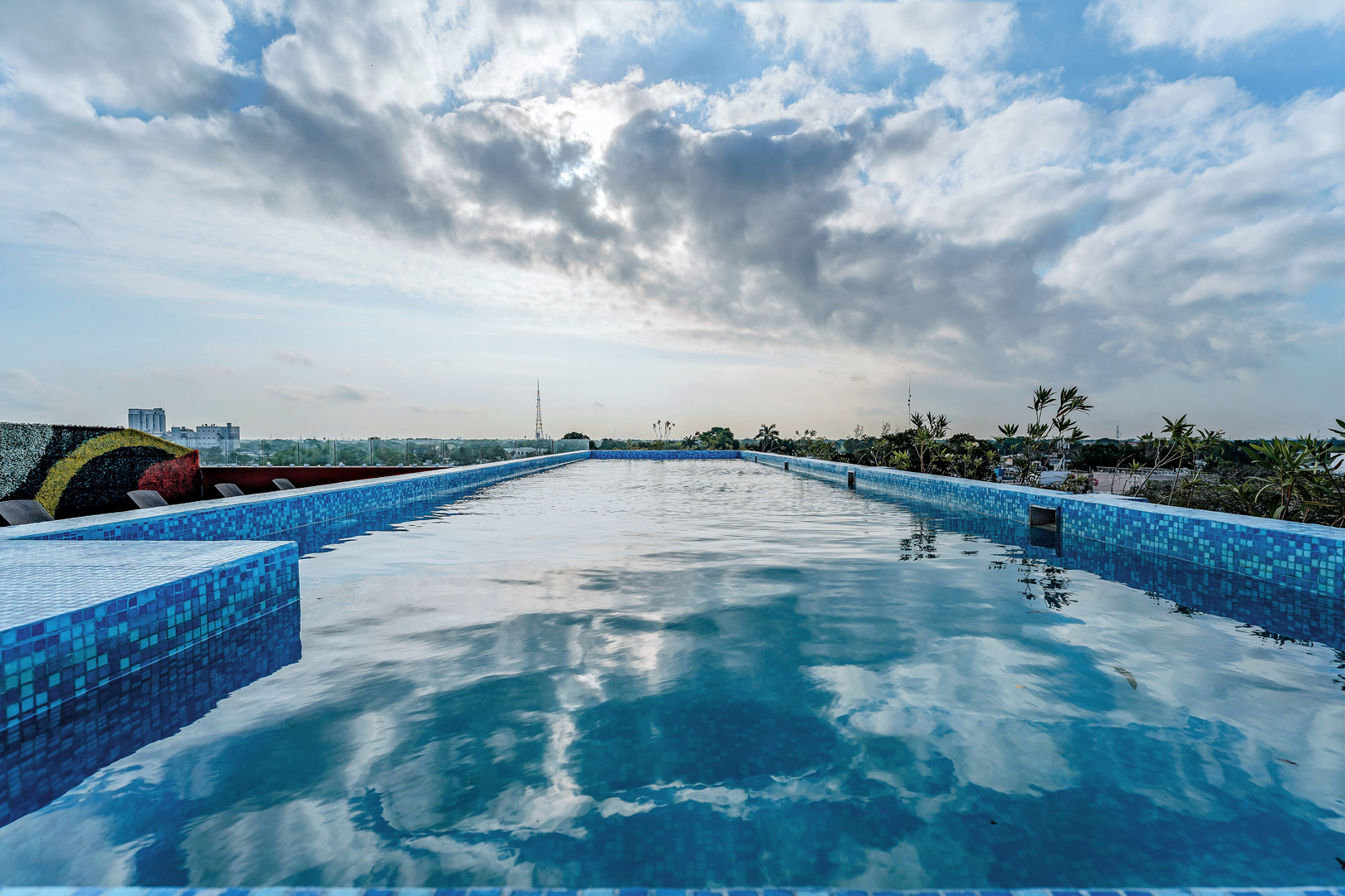 Piscina en la azotea bajo un cielo nublado. Su piscina de azulejos azules refleja el cielo.