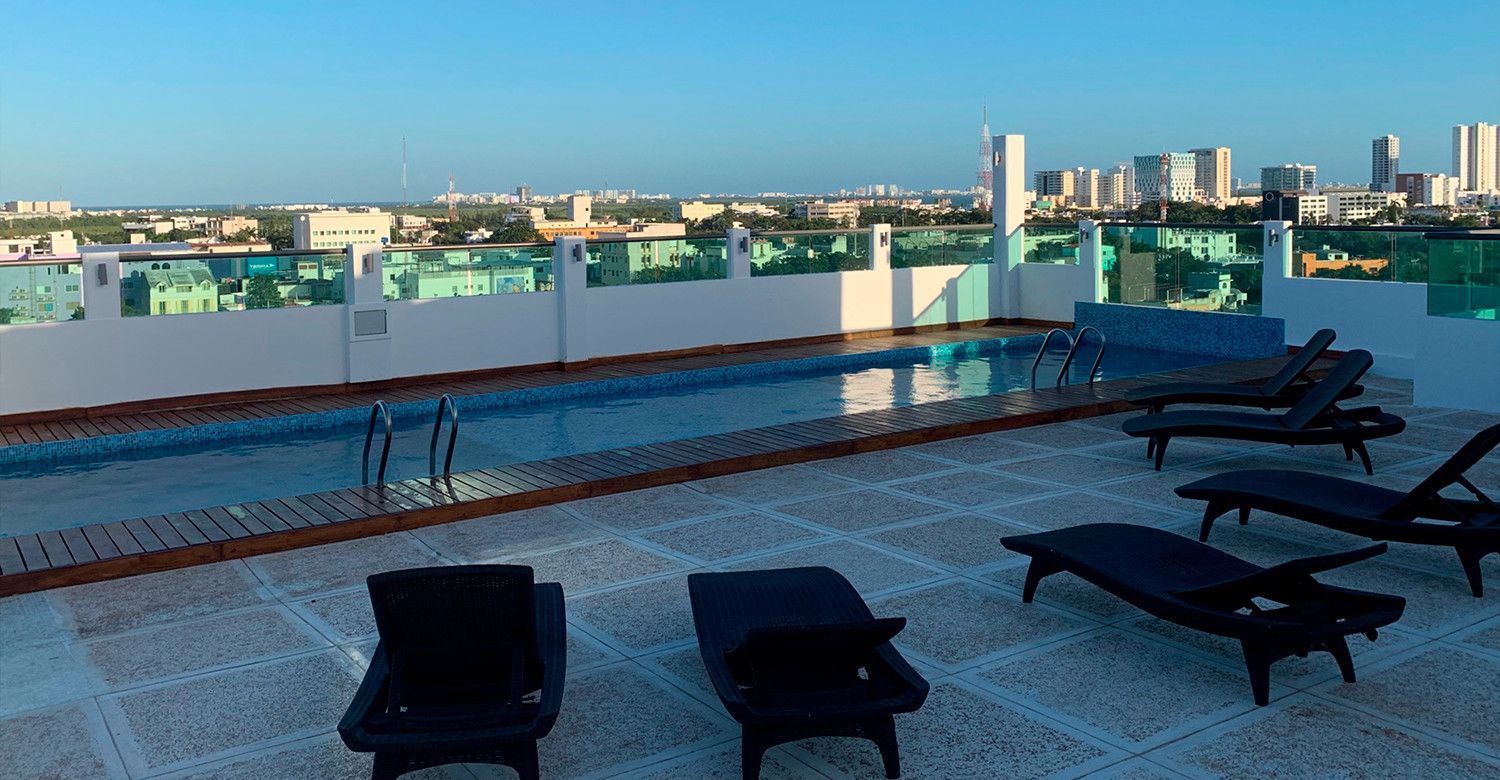 Piscina en la azotea con tumbonas y vistas al paisaje urbano. Cielo azul, agua y un edificio.