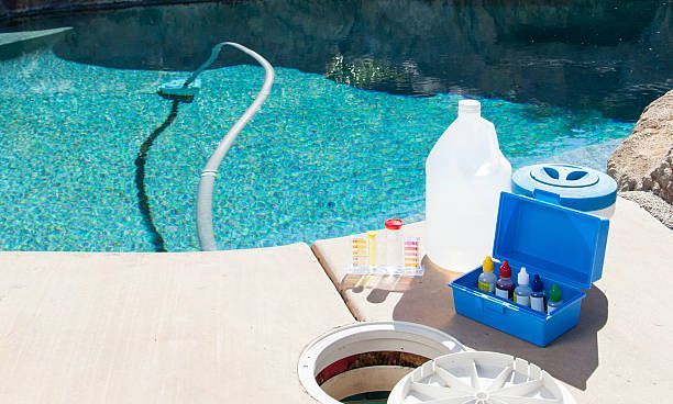 Poolside view of pool cleaning supplies: hose, chemicals, test kit. Turquoise water.