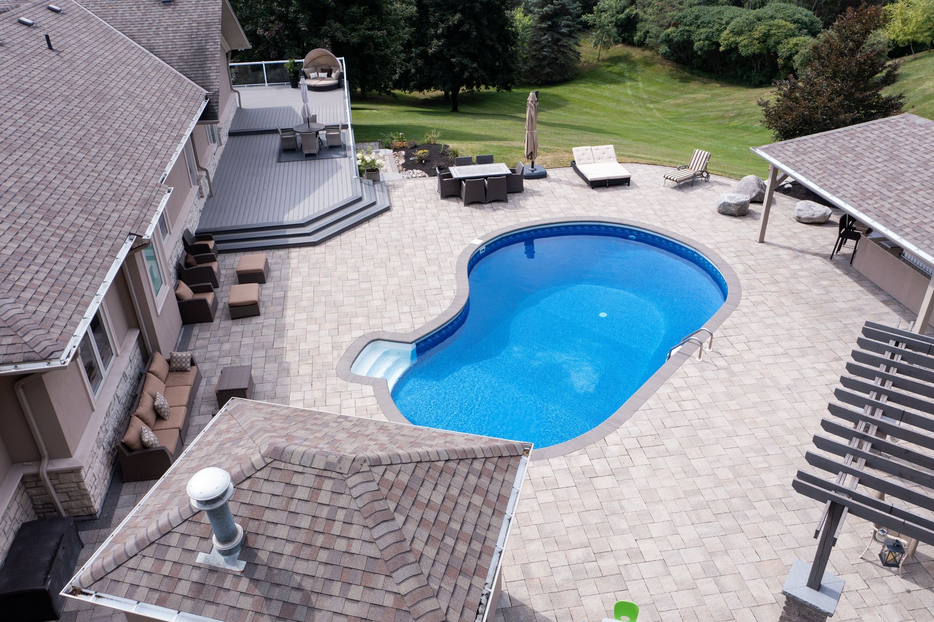 Backyard patio with a blue swimming pool, lounge chairs, and a grill beside a house