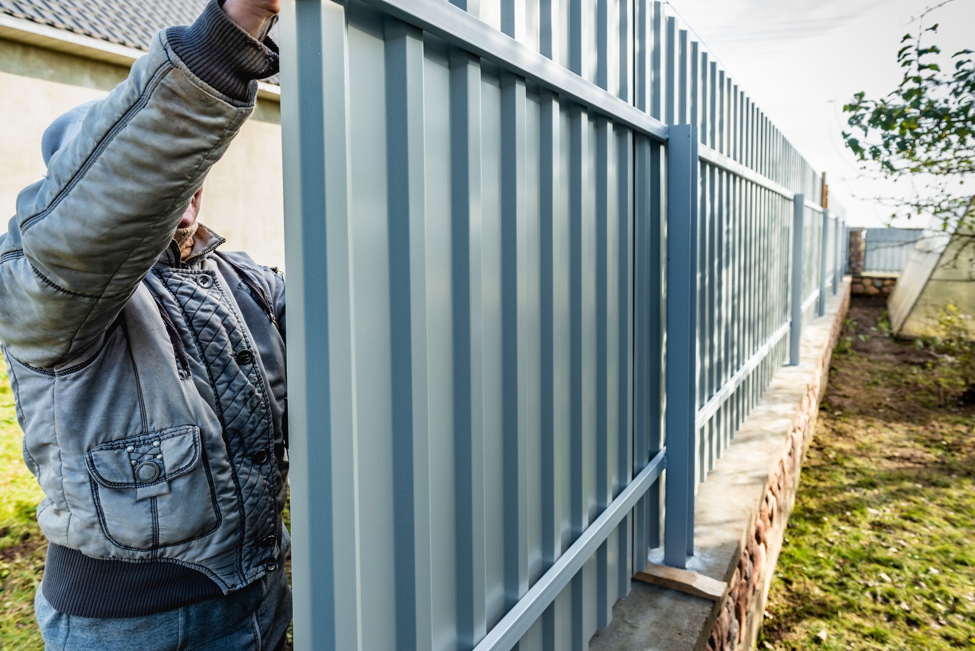A worker installs a corrugated metal fence during a professional commercial fencing installation. A worker installs a corrugated metal fence during a professional commercial fencing installation.