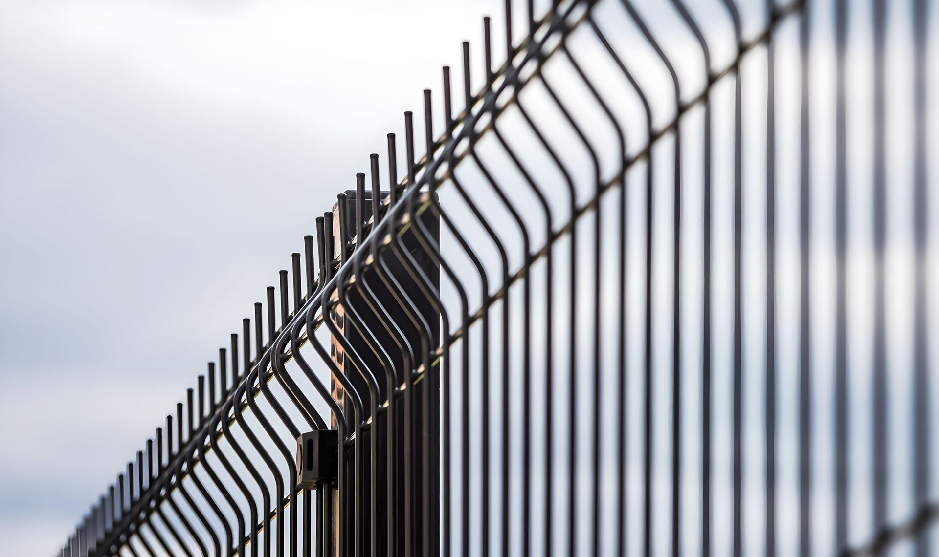 Close-up of a black metal security fence with vertical bars against a blurred sky.
