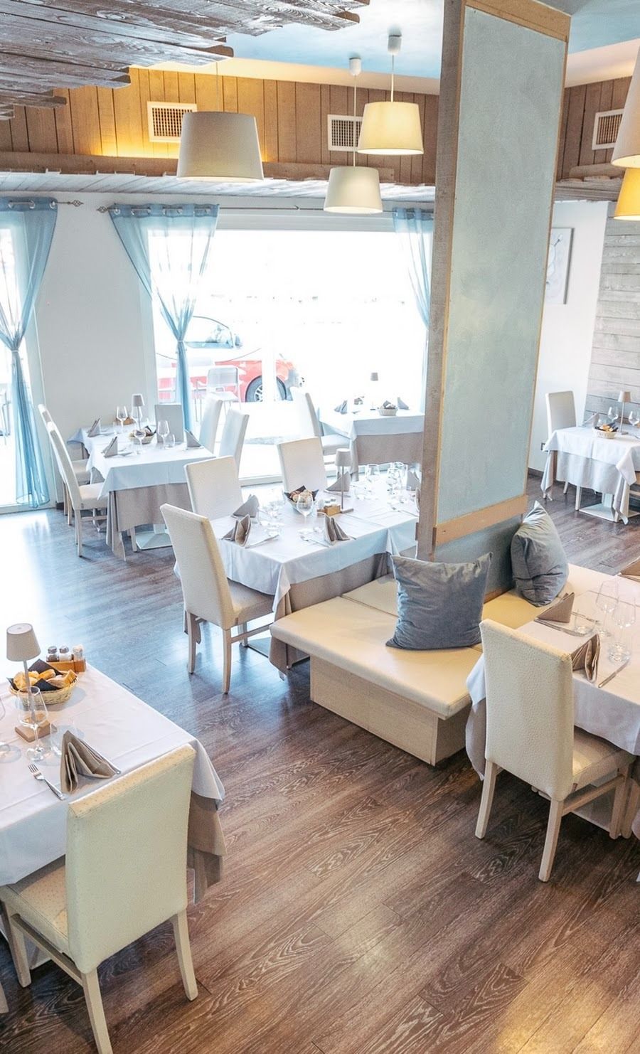 Una sala da pranzo del ristorante, luminosa e ben illuminata, con tavoli e sedie apparecchiati con tovaglie bianche e delicati dettagli blu su pavimenti in legno.