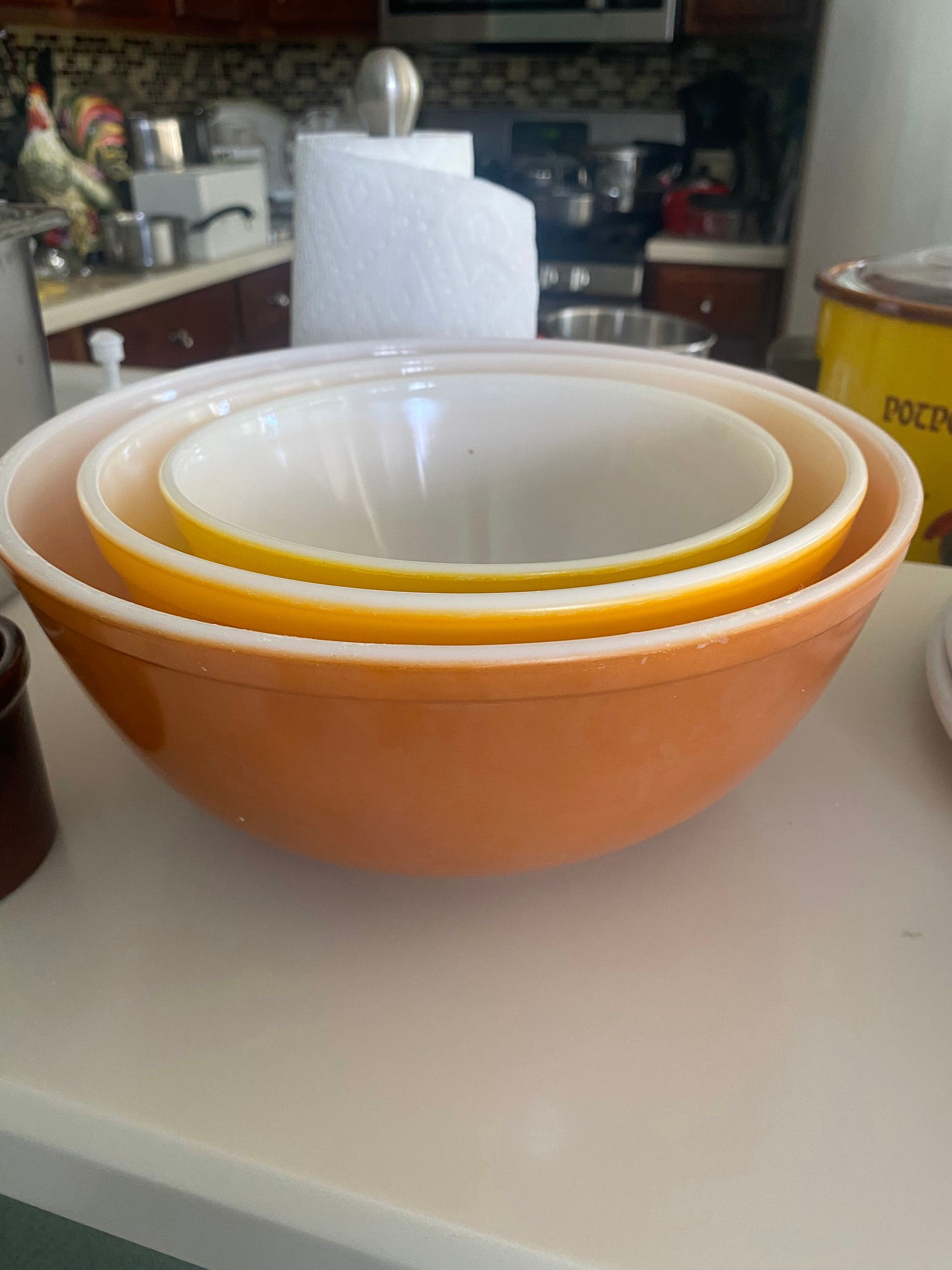 Three nesting orange and white mixing bowls on a counter, kitchen in the background.