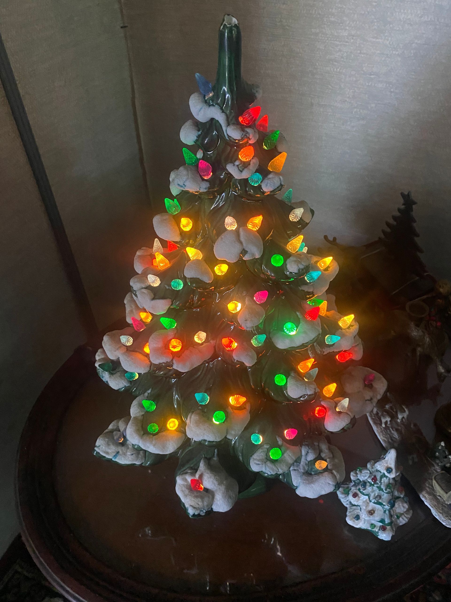 Lit ceramic Christmas tree on a table, with colorful lights and fake snow.