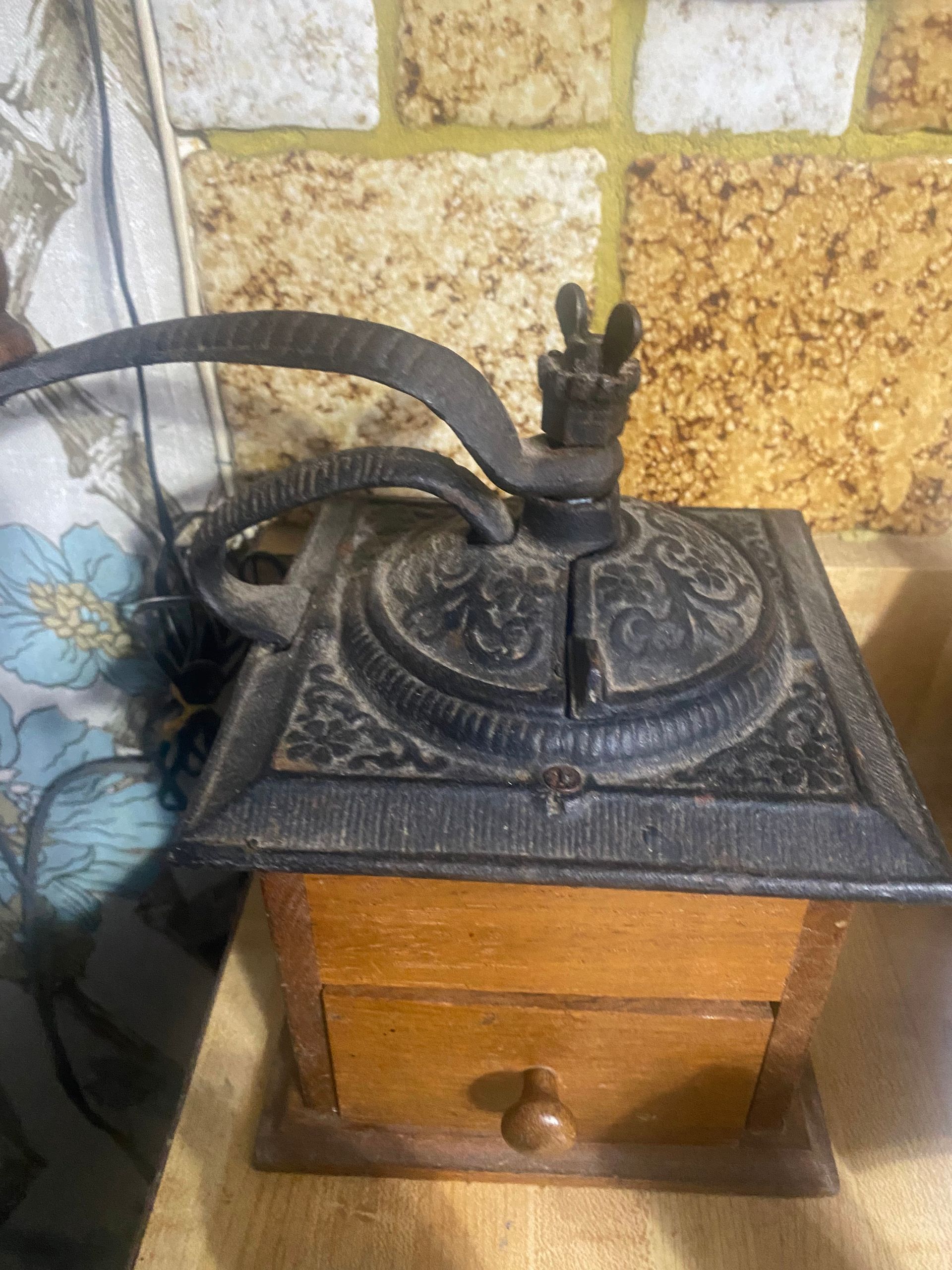 Antique cast iron and wood coffee grinder with handle and drawer on a wooden surface.