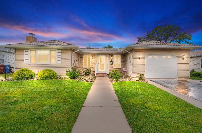 Ranch-style house with green lawn, sidewalk, and cloudy blue and pink sky.