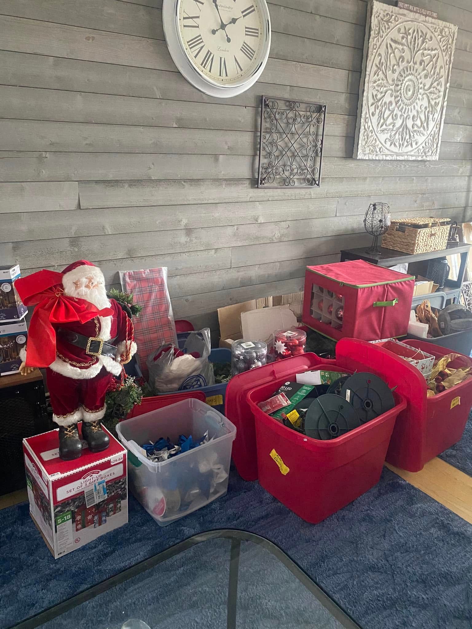 Santa figure next to Christmas decorations and red storage bins near a wall and rug.