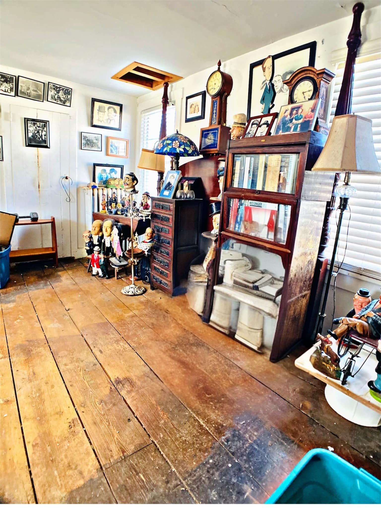 Cluttered room with wooden floors, antique furniture, and various objects on display.