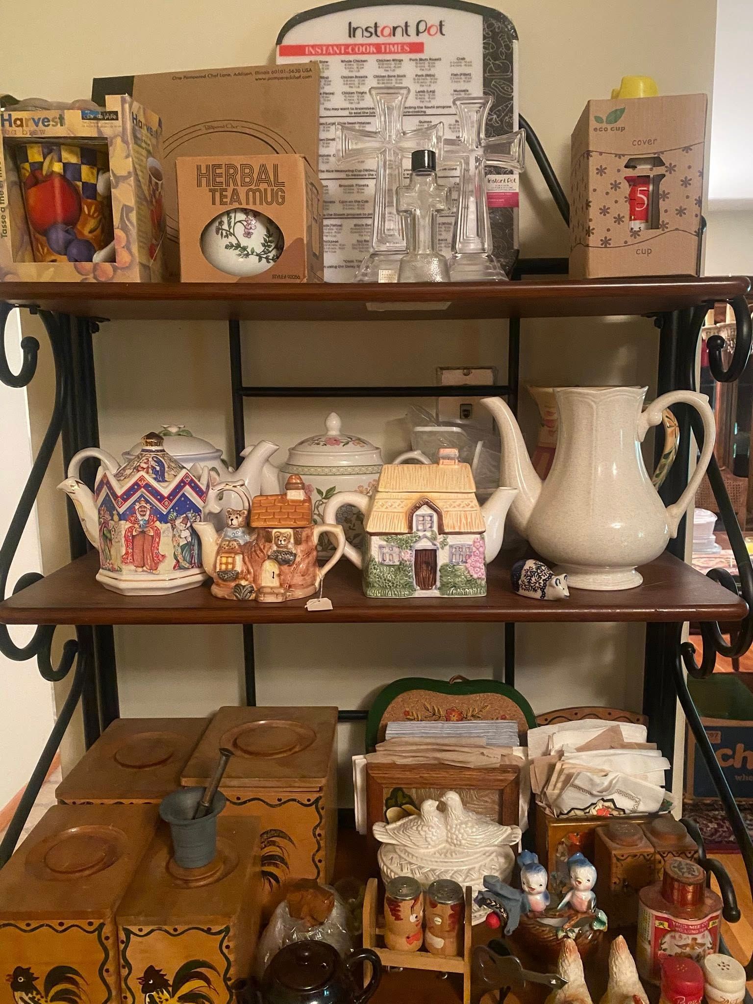 A three-tiered shelf displays teapots, decorative boxes, and glassware against a light-colored wall.