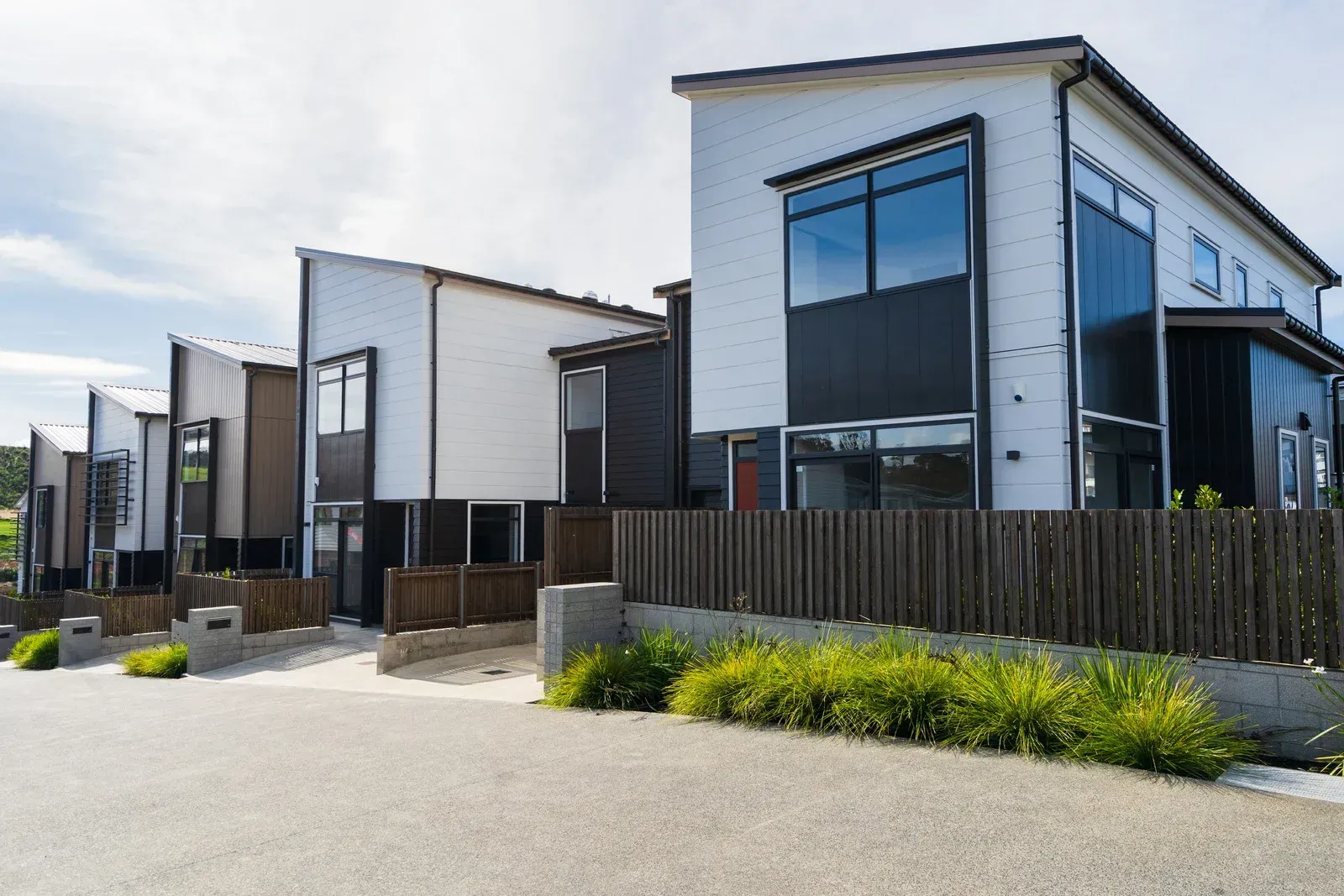 Row of modern townhouses with black and white facades and a wooden fence.