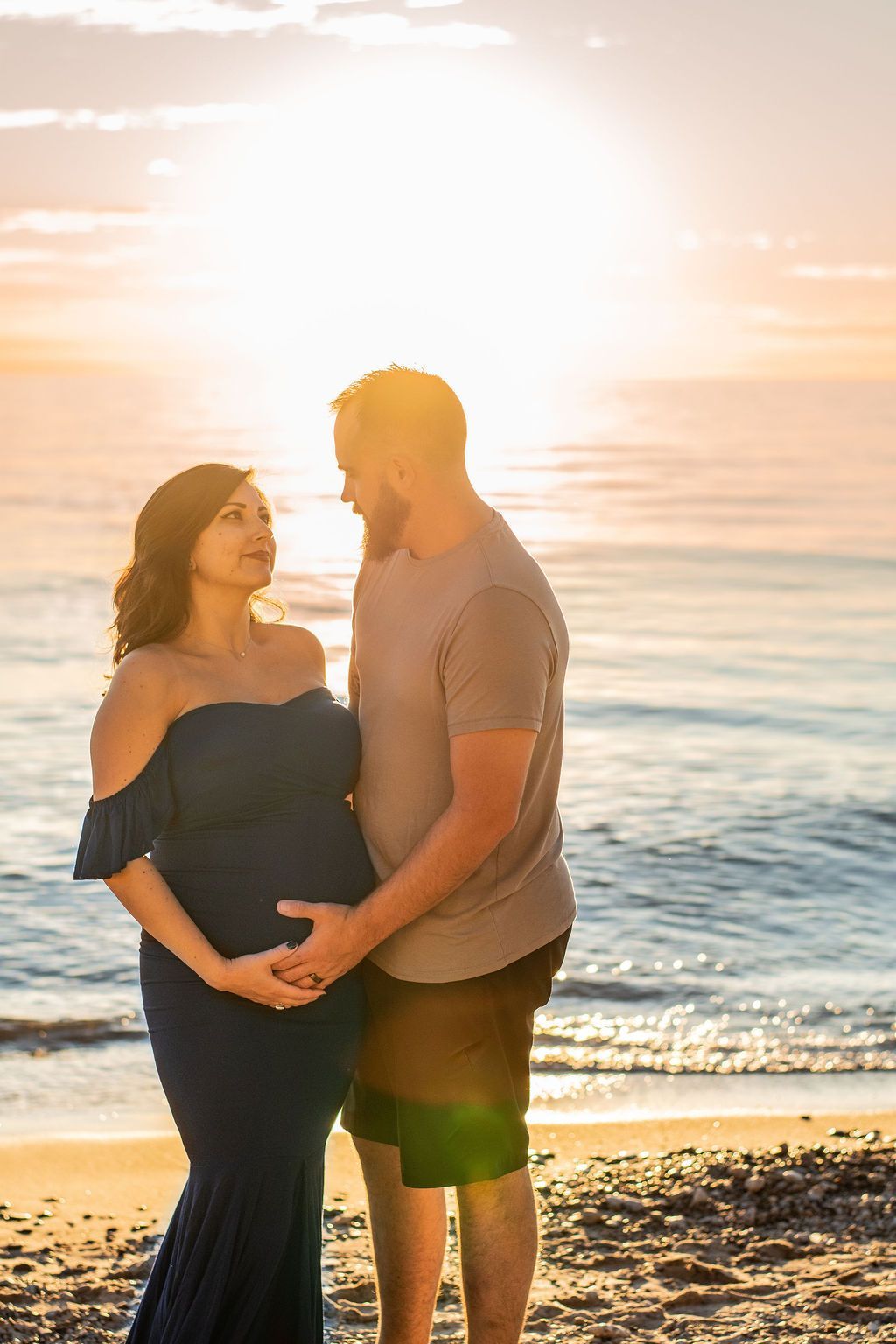 Couple holding hands at sunset on a beach, backlit by the golden sun.
