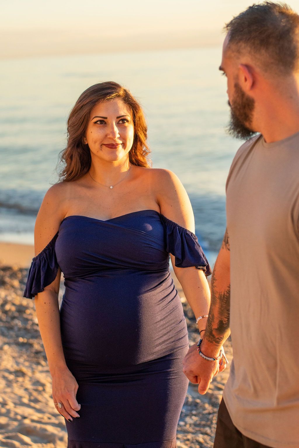 Two people standing on a beach at sunset, facing each other and holding hands