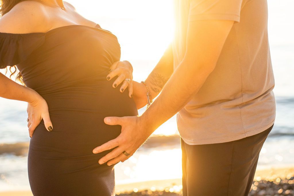 Pregnant woman and partner holding her belly at sunset on the beach
