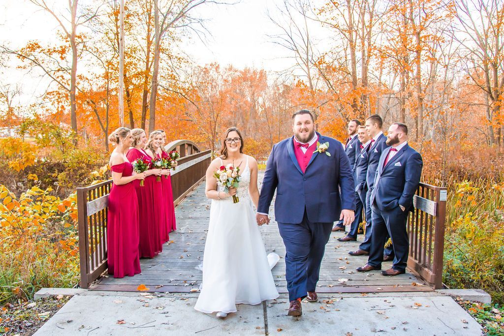 Wedding couple walking on a bridge with bridesmaids and groomsmen in autumn scenery