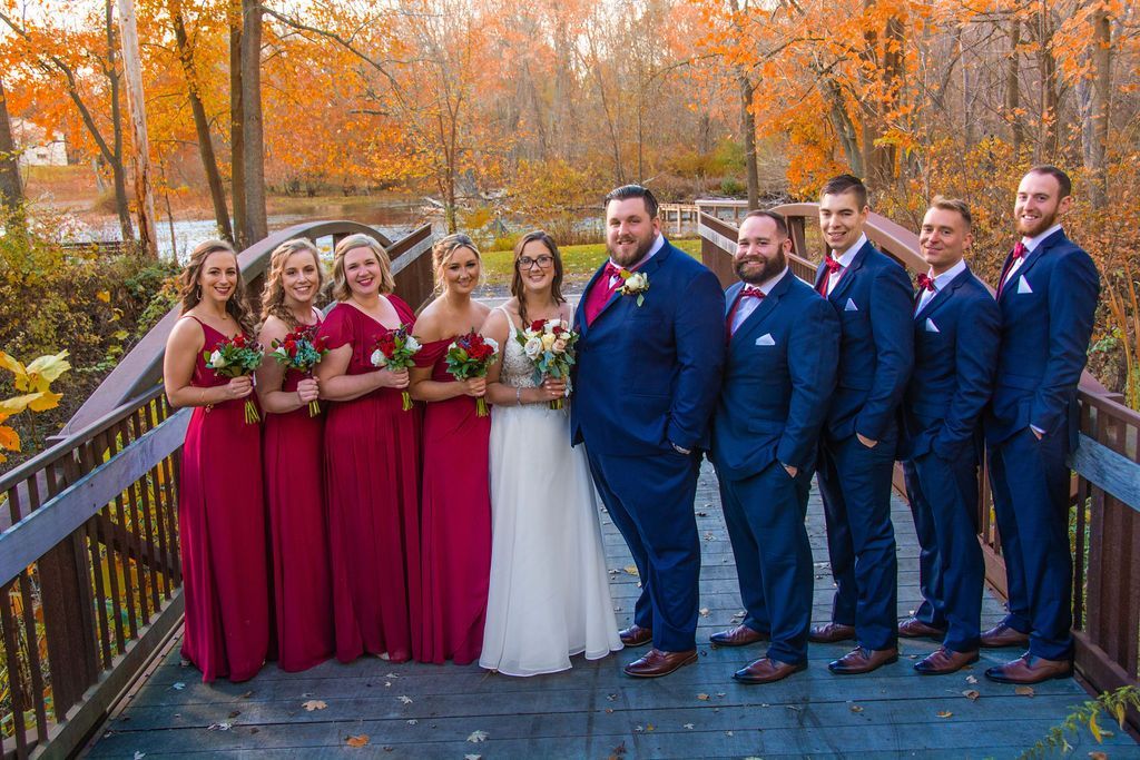 Wedding party on a wooden bridge in autumn, bridesmaids in burgundy and groomsmen in blue suits, bride in white.