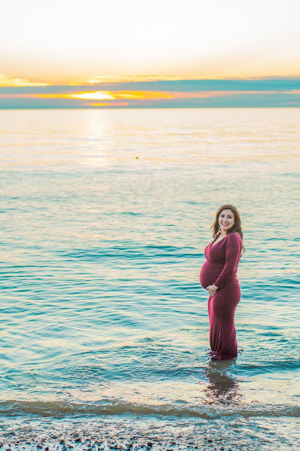 Person in a red dress standing in shallow water at sunset by the ocean