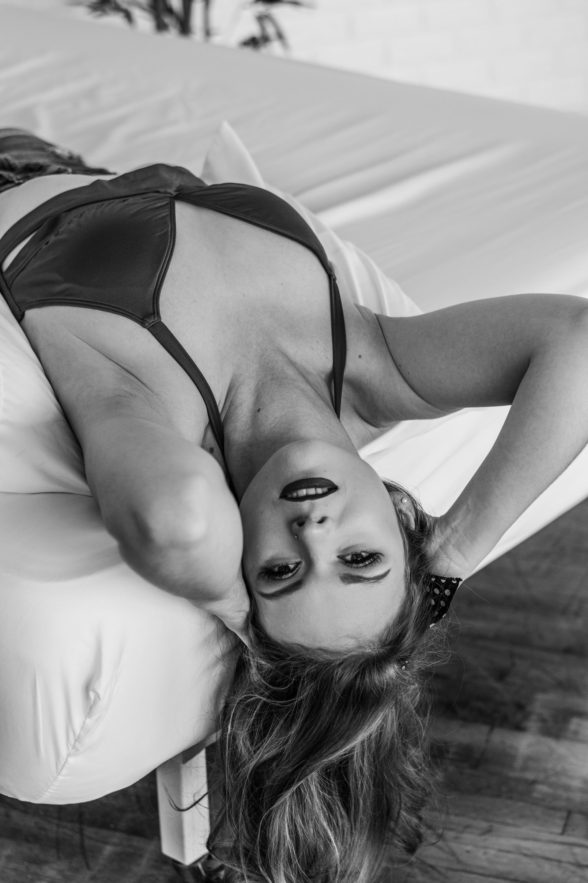 Woman in a dark top reclining on a bed, looking at the camera.