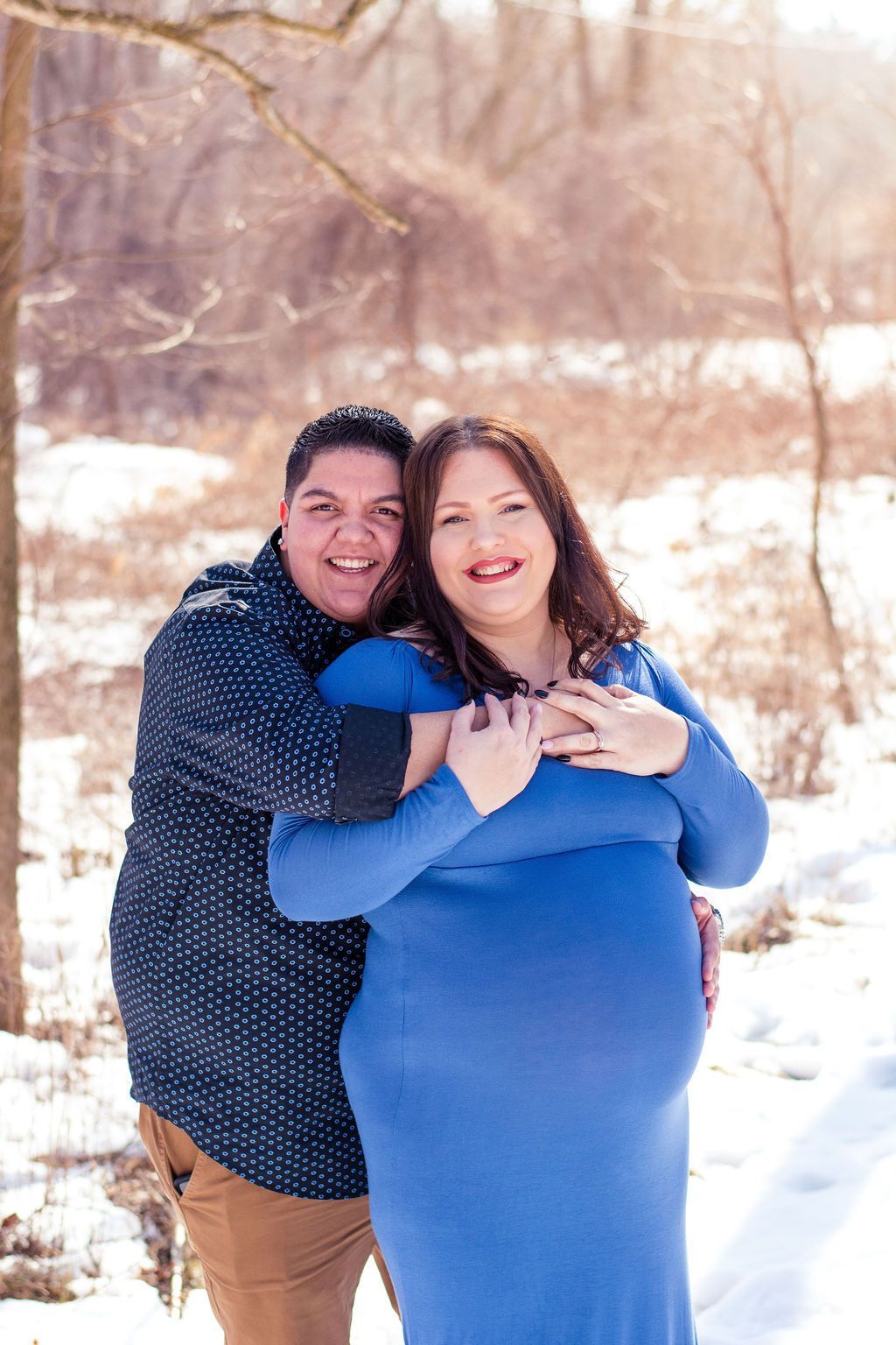Two people hugging outdoors in snow, smiling in blue and brown winter clothes