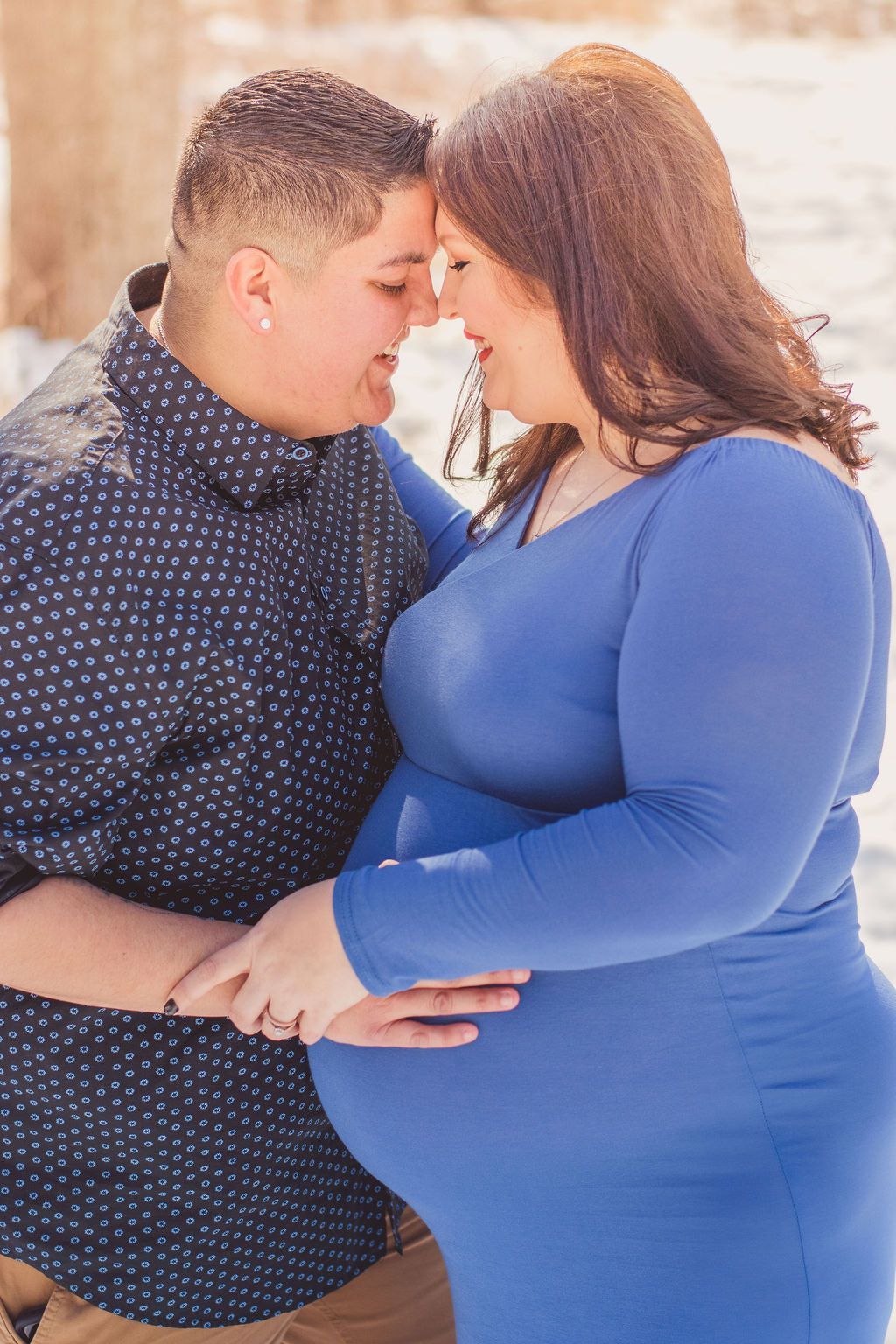 Couple embracing gently, foreheads touching, with the woman in a blue dress and the man in a dark patterned shirt.