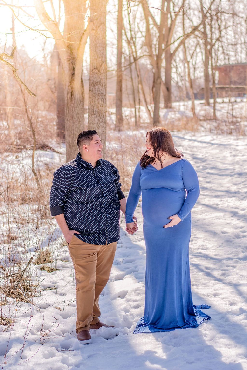 Two people walking together on a snowy path in a leafless winter park, smiling at each other.