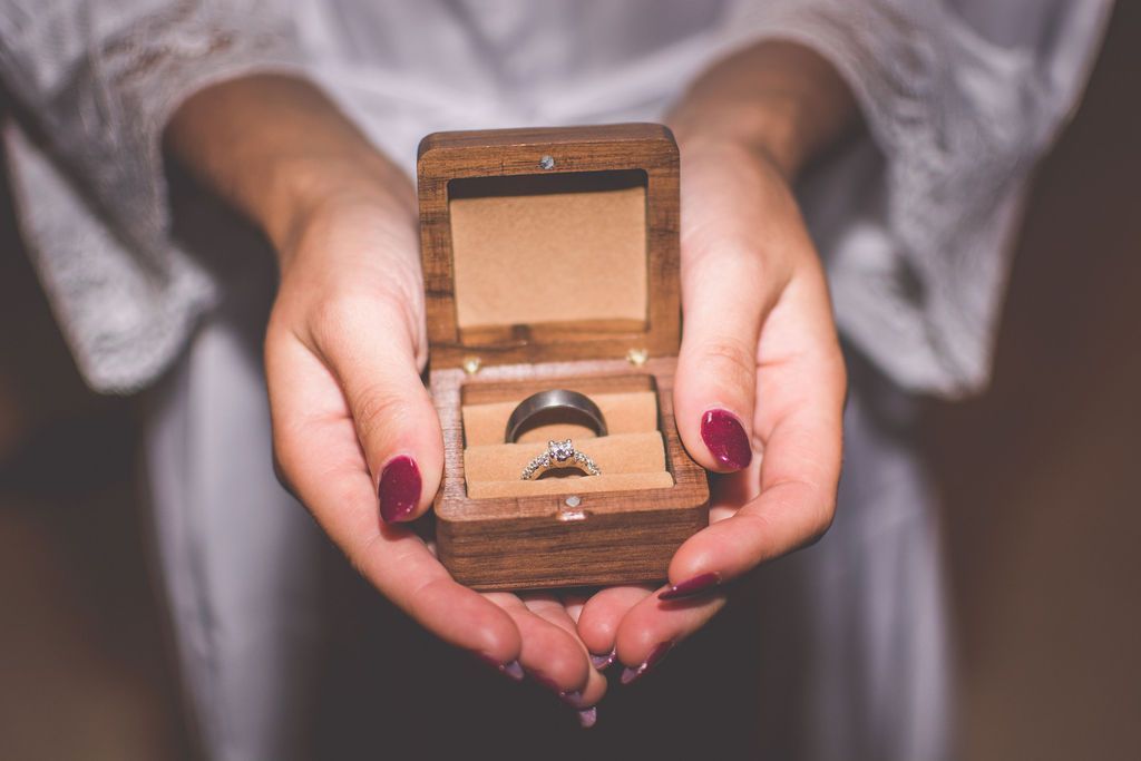 Hands holding an open wooden ring box with a ring inside and water dripping below