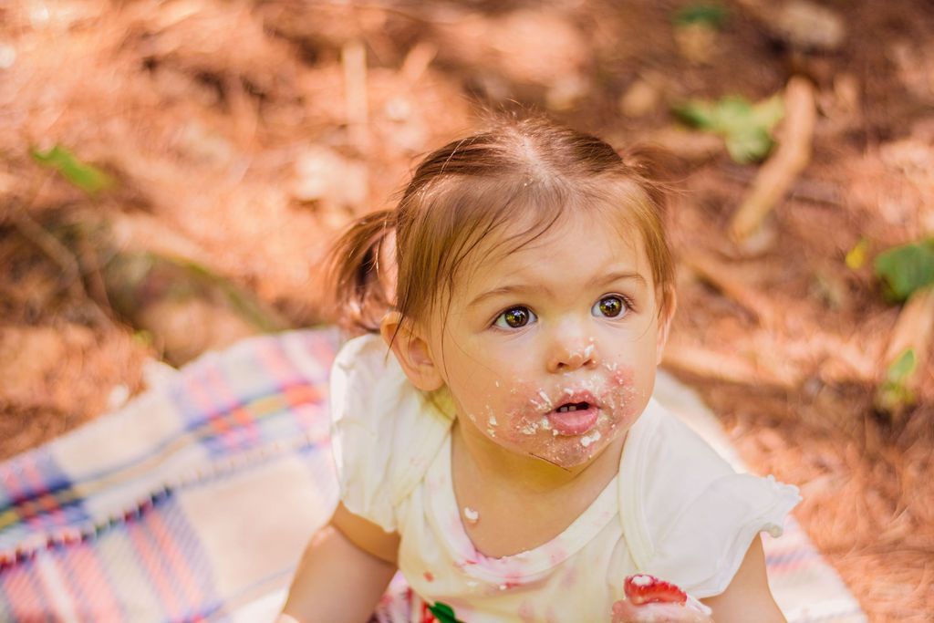 Toddler sitting on a blanket outdoors, looking up with a messy face and white shirt